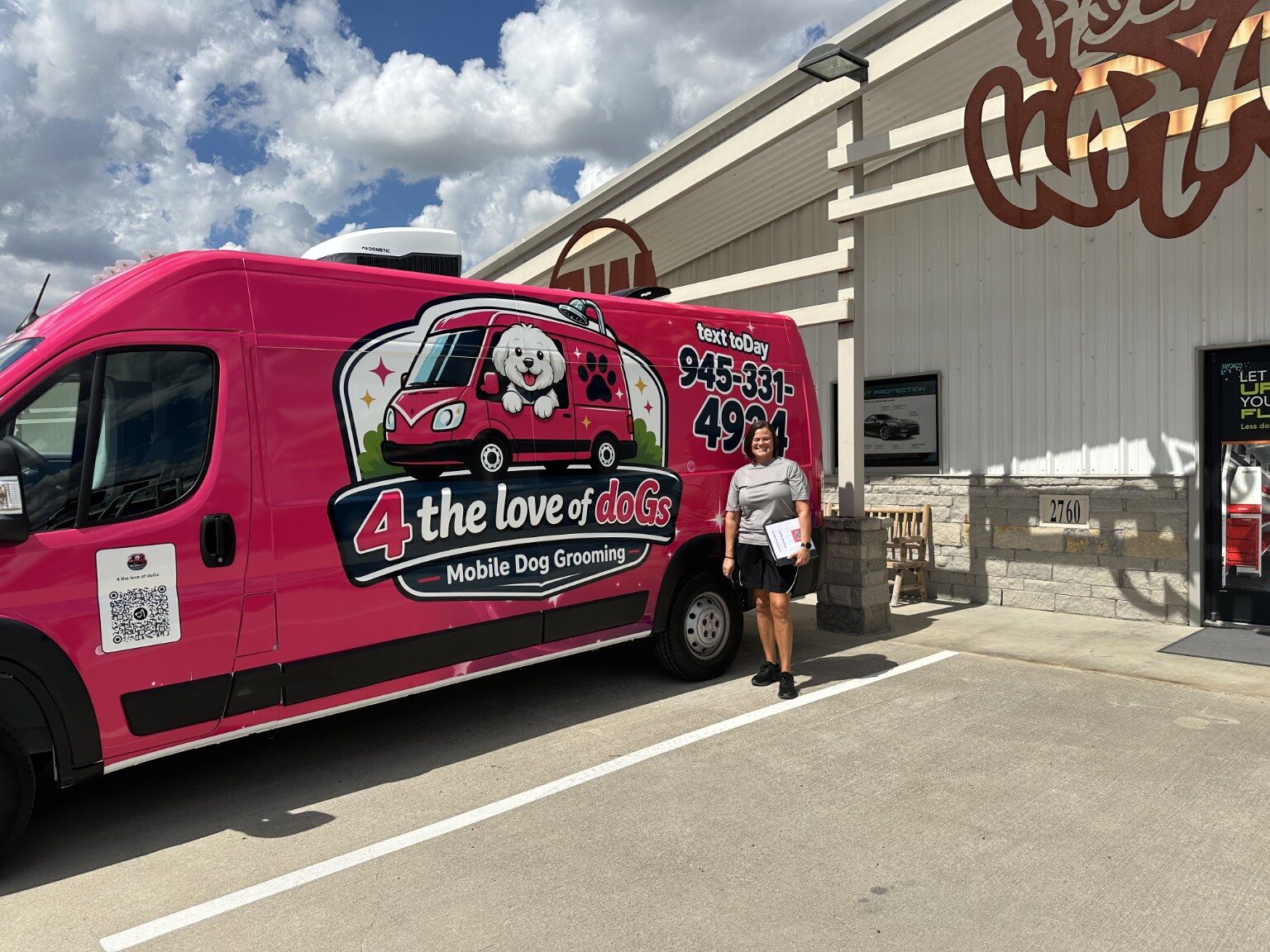 Whitney standing beside the bright pink 4 the Love of doGs mobile grooming van